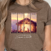 Load image into Gallery viewer, Brown t-shirt with a Christmas nativity scene graphic and text worn by a person.