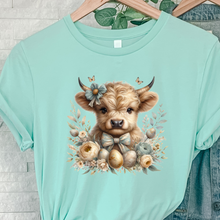 Load image into Gallery viewer, Mint green t-shirt with a cute Highland cow illustration with flowers and Easter eggs