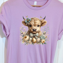 Load image into Gallery viewer, Purple t-shirt with a cute Highland cow illustration of Easter eggs and floral elements 