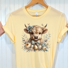 Load image into Gallery viewer, French vanilla Bella Canvas t-shirt with a Highland cow design with Easter eggs and flowers