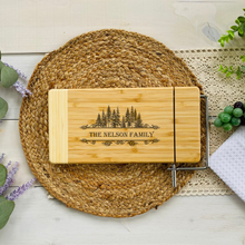Load image into Gallery viewer, Personalized Bamboo Cutting Board With Family Name Framed With Pine Trees Cheese Slicer On End 