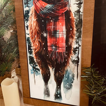 Load image into Gallery viewer, Painting of a cow wearing a plaid scarf in a snowy forest setting, framed with Christmas decor.