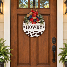 Load image into Gallery viewer, Black-and-white cow print round “Howdy” door hanger with red bandana bows and greenery.