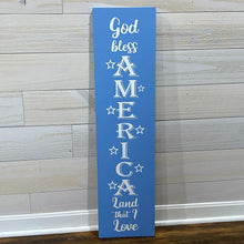 Load image into Gallery viewer, Vertical wooden sign with &#39;God bless America Land that I Love&#39; text on a blue background against a wooden wall.