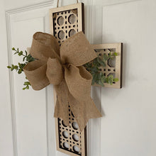 Load image into Gallery viewer, Decorative wall hanging rattan cross with a burlap bow and greenery on a white door.