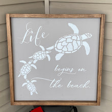 Load image into Gallery viewer, Decorative sign with turtles and &#39;Life begins on the beach&#39; text in a wooden frame.