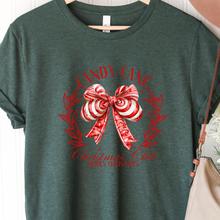 Load image into Gallery viewer, Green t-shirt with a red candy cane bow design on a hanger against a white background.
